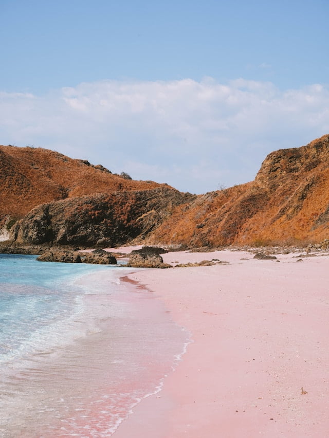 a pink beach with blue water and hills in Komodo